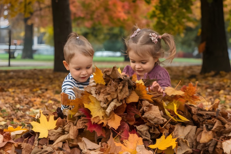 Two young children playing with autumn leaves in a park